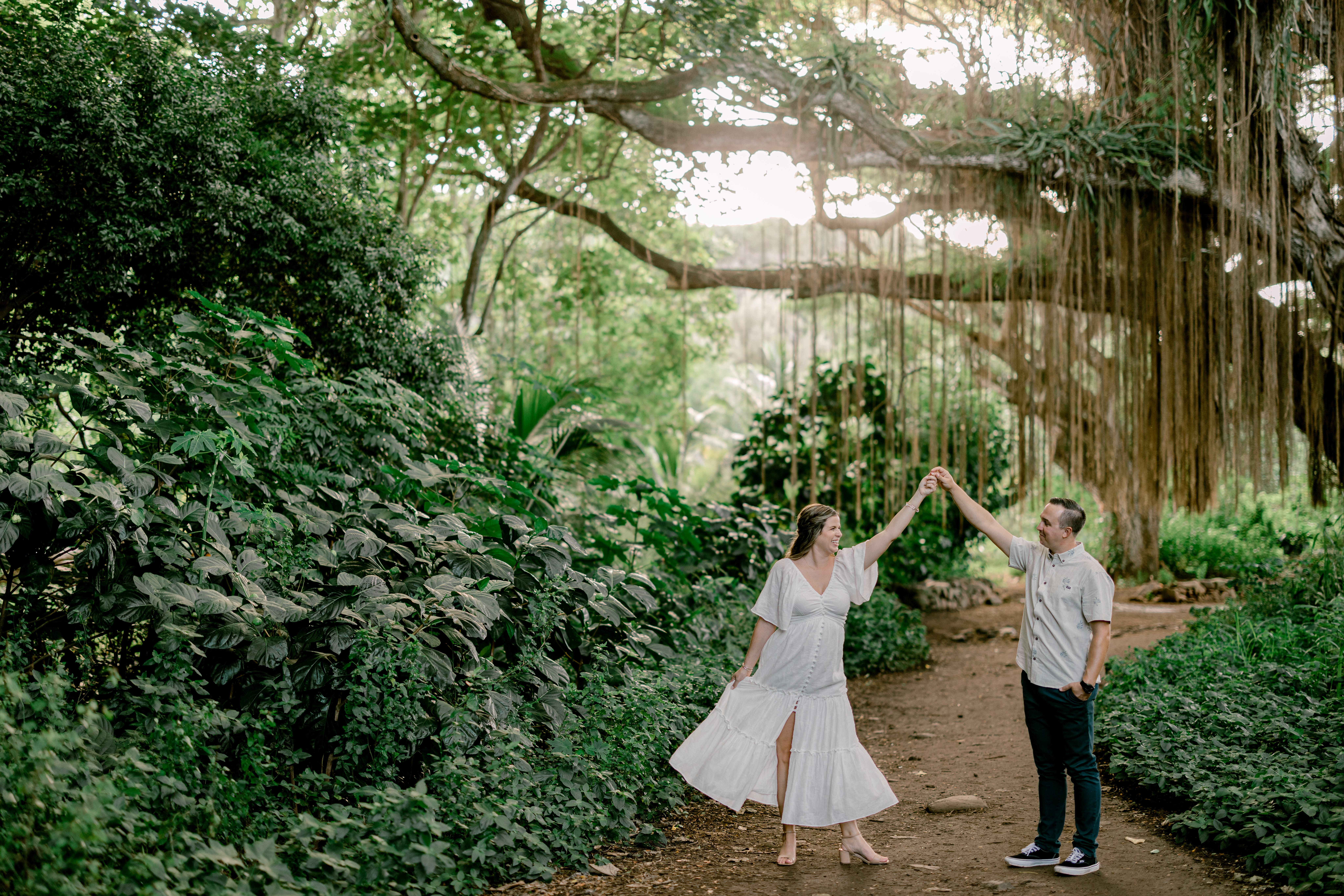 Maui Engagement Photography Session at Honolua Forest of guy and girl holding hands in the air and girl fanning her dress.
