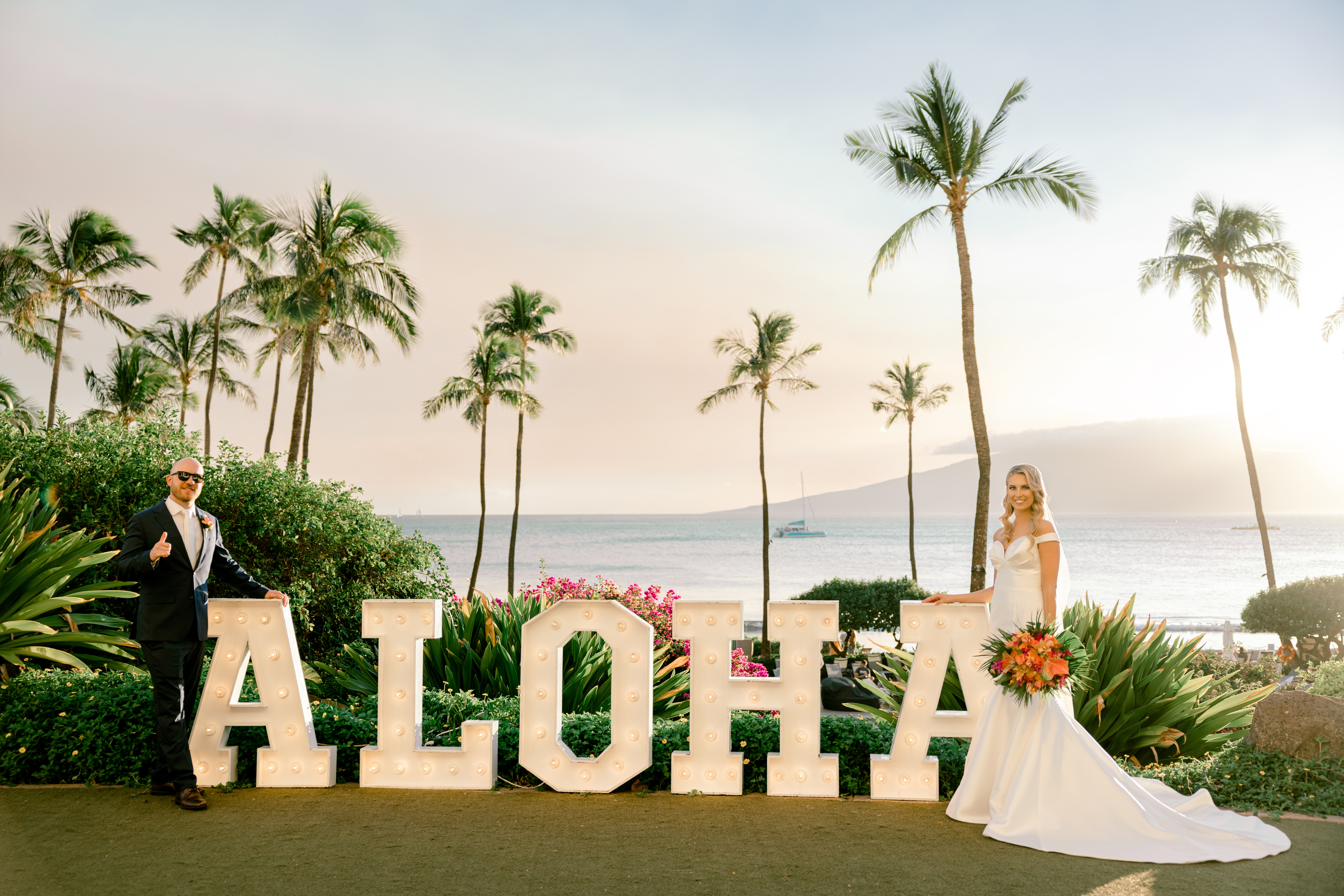 Bride and groom standing in front of the Maui Hyatt's ALOHA sign with palm trees in the background