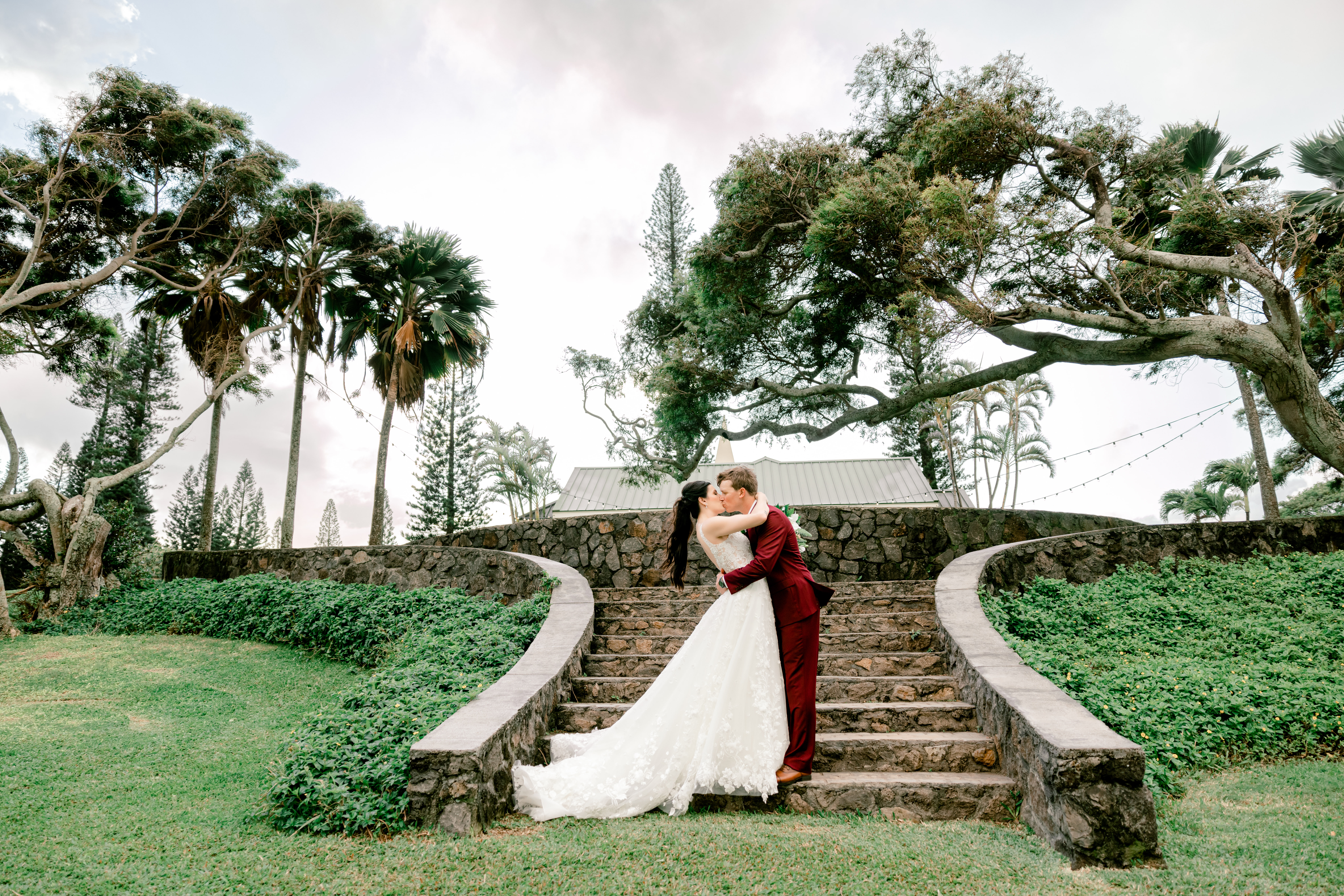 Newlyweds kissing while standing at the bottom of the stairs at the Kapalua Pineapple Chapel