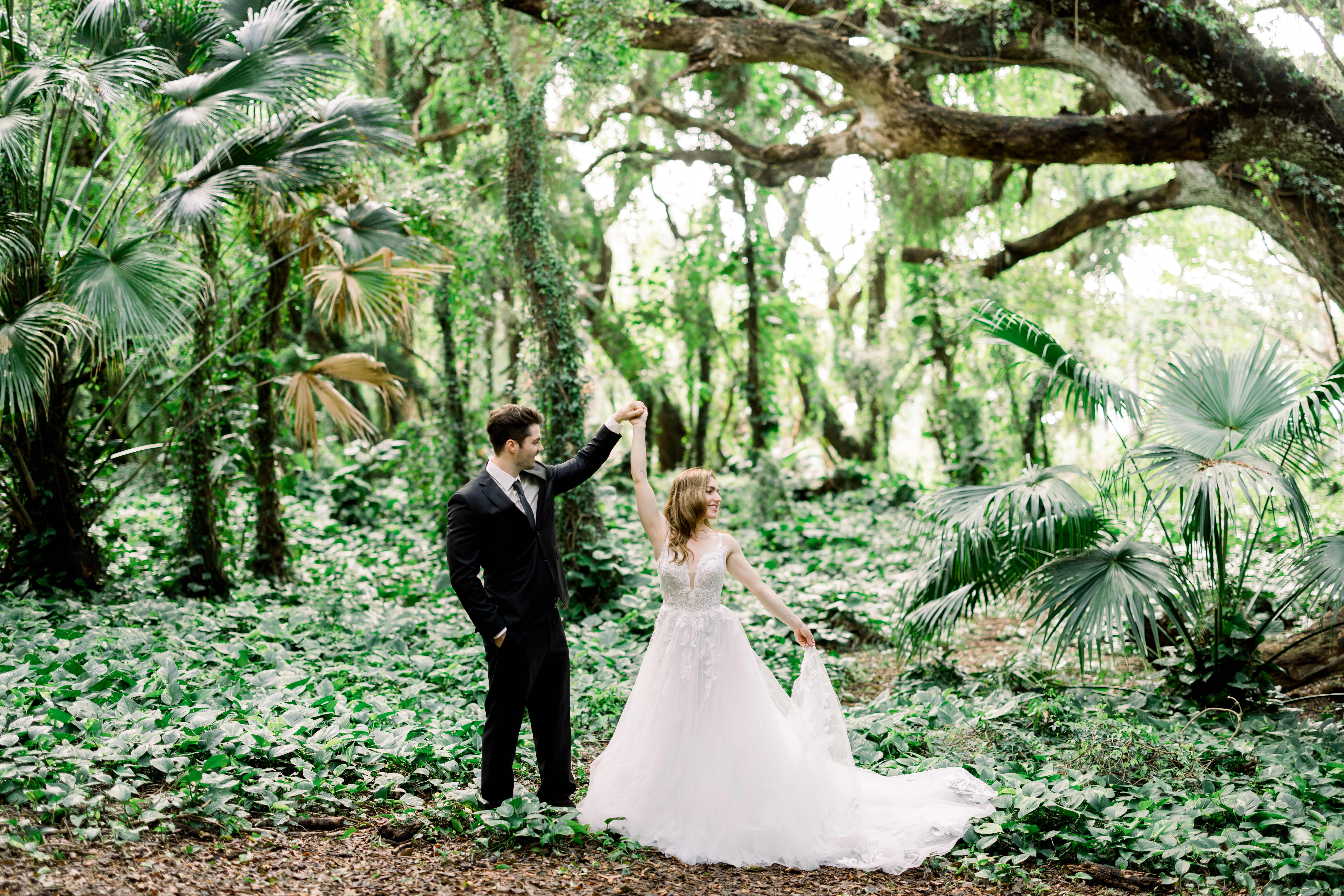 Couple at tropical forest in Maui holding hands over head while woman using other hand to hold the bottom of her wedding dress