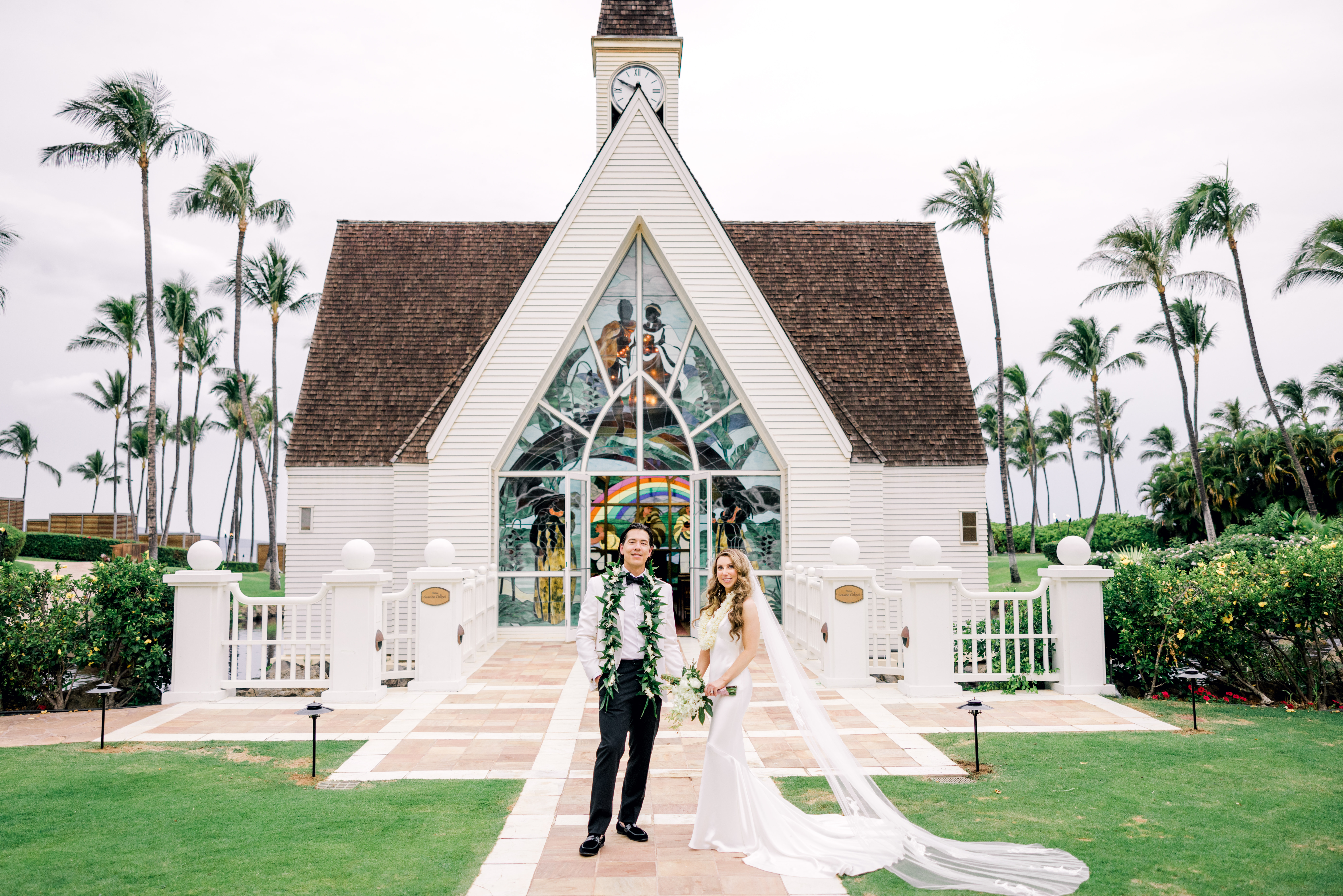Woman in wedding dressing with man in white dress shirt and black pants standing in front of a church at the Grand Wailea hotel in Maui.