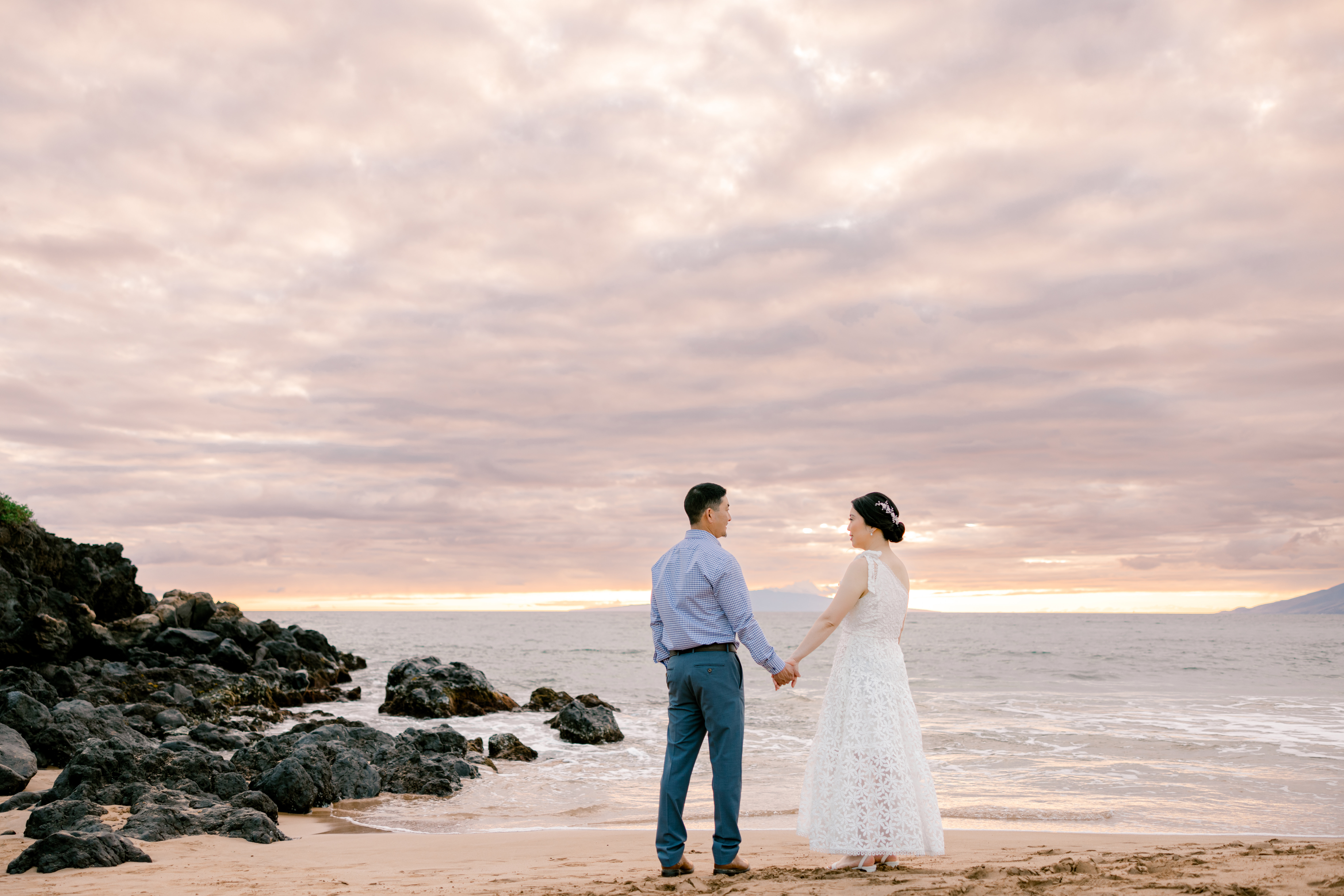 Man and woman standing in sand holding hands during sunset in Maui
