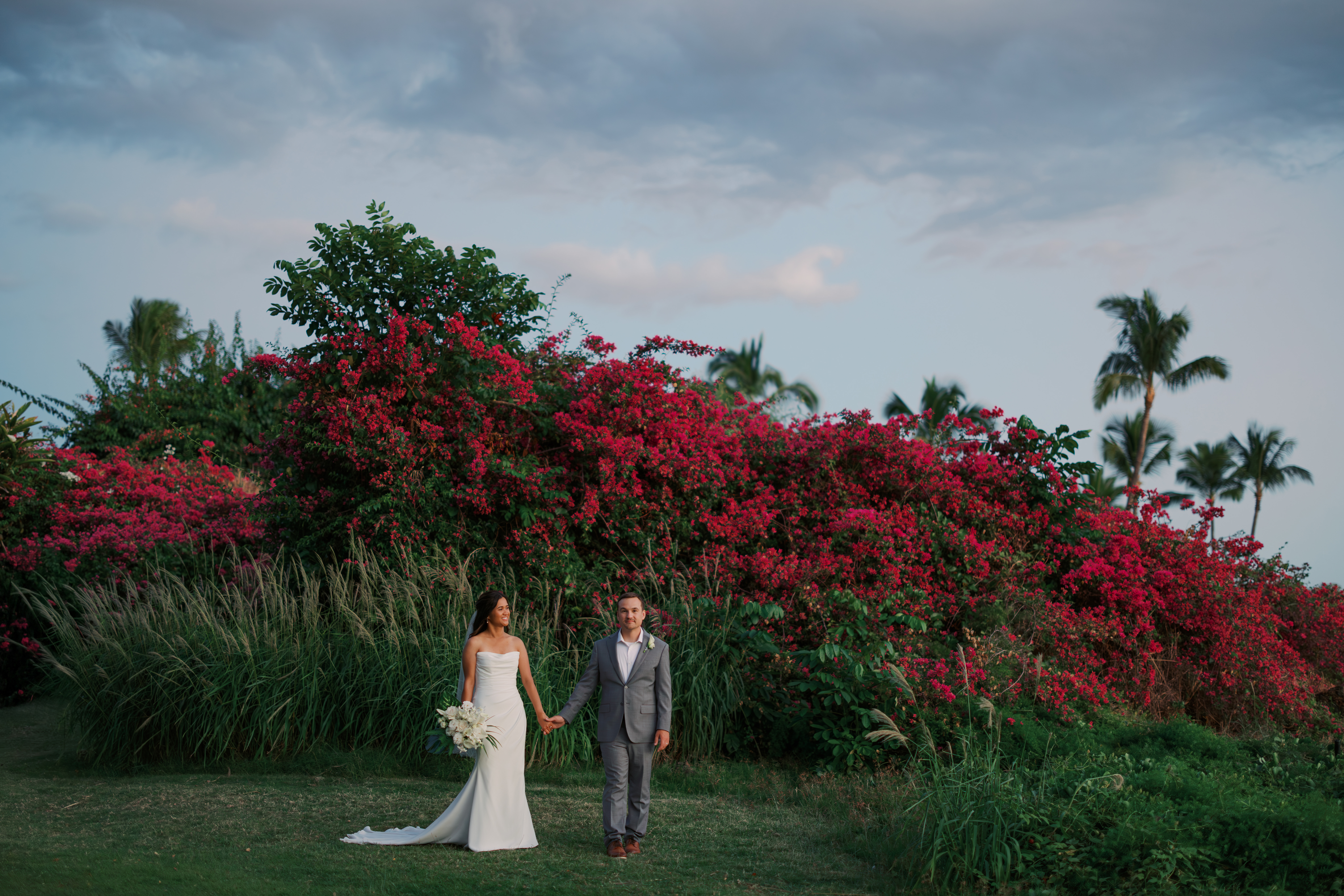 Woman wearing a white wedding dress and man wearing a grey suit holding hands at wedding venue Gather on Maui