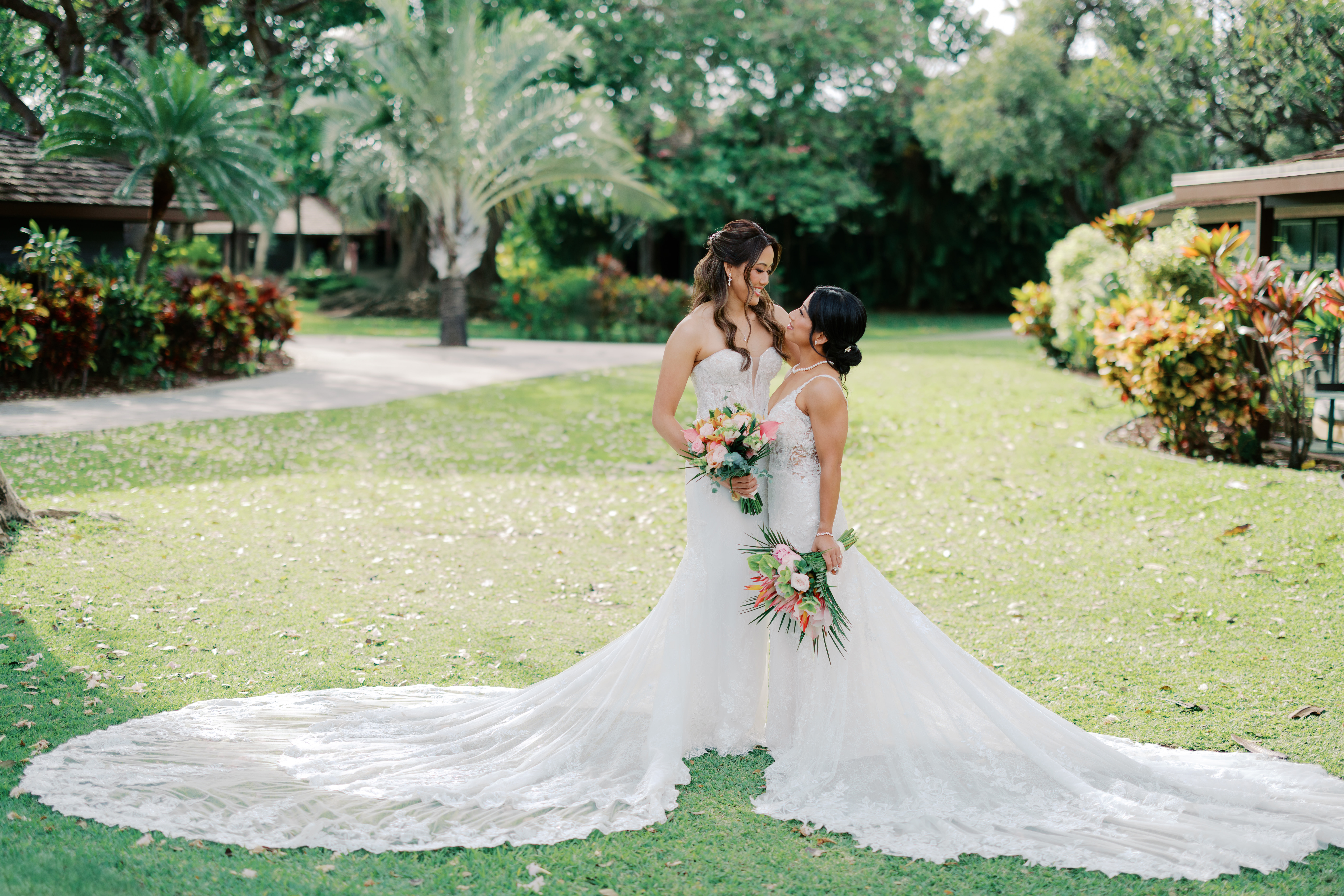 Two women wearing wedding dresses standing side by side looking face to face holding bouquets at Royal Lahaina Resort Wedding Venue in Maui, Hawaii